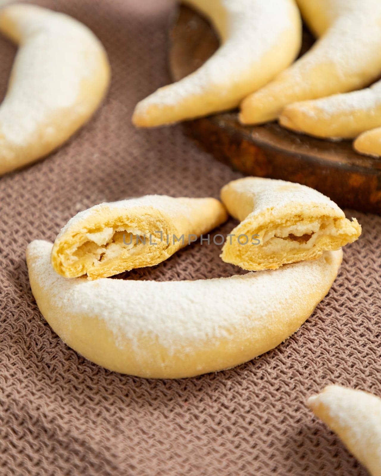 Crescent shaped cookies with a sweet filling are dusted with powdered sugar and displayed on a brown cloth