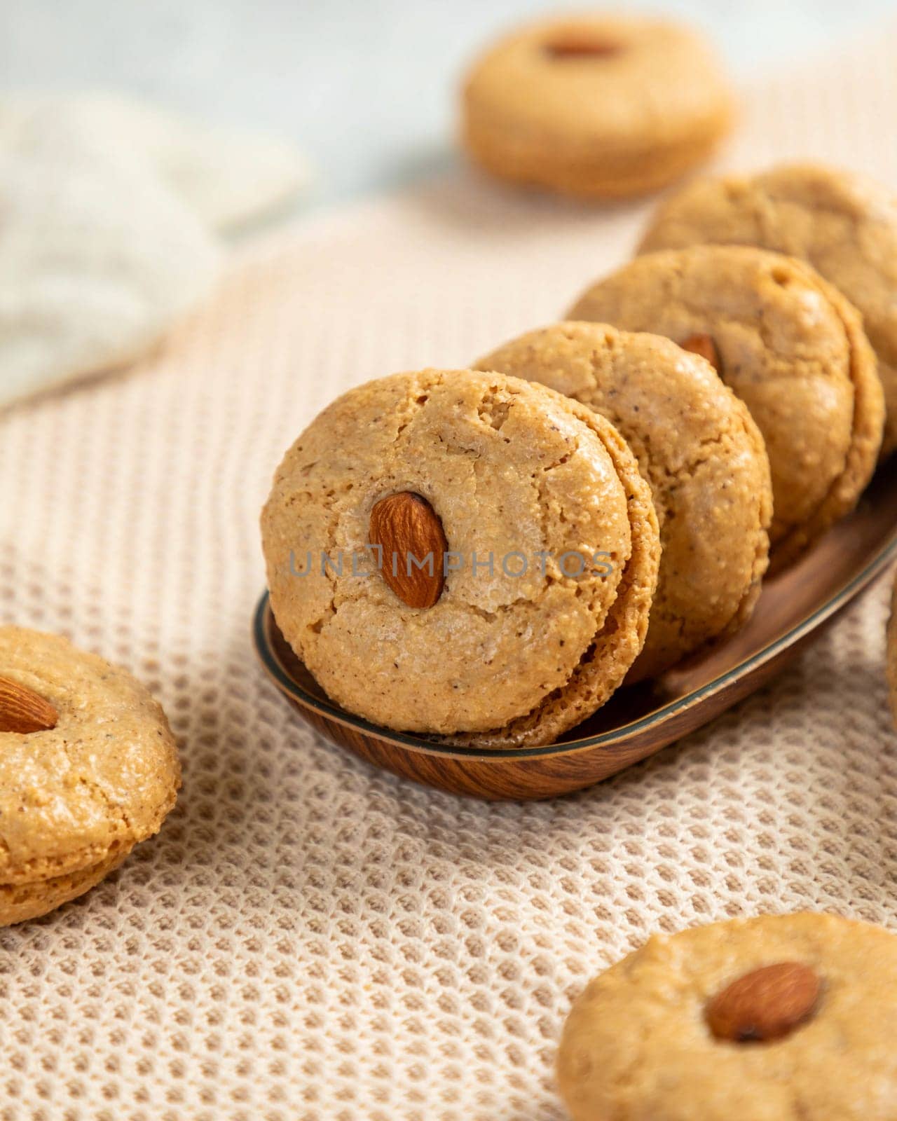 Freshly baked macarons with almonds are arranged on a wooden tray and a beige tablecloth