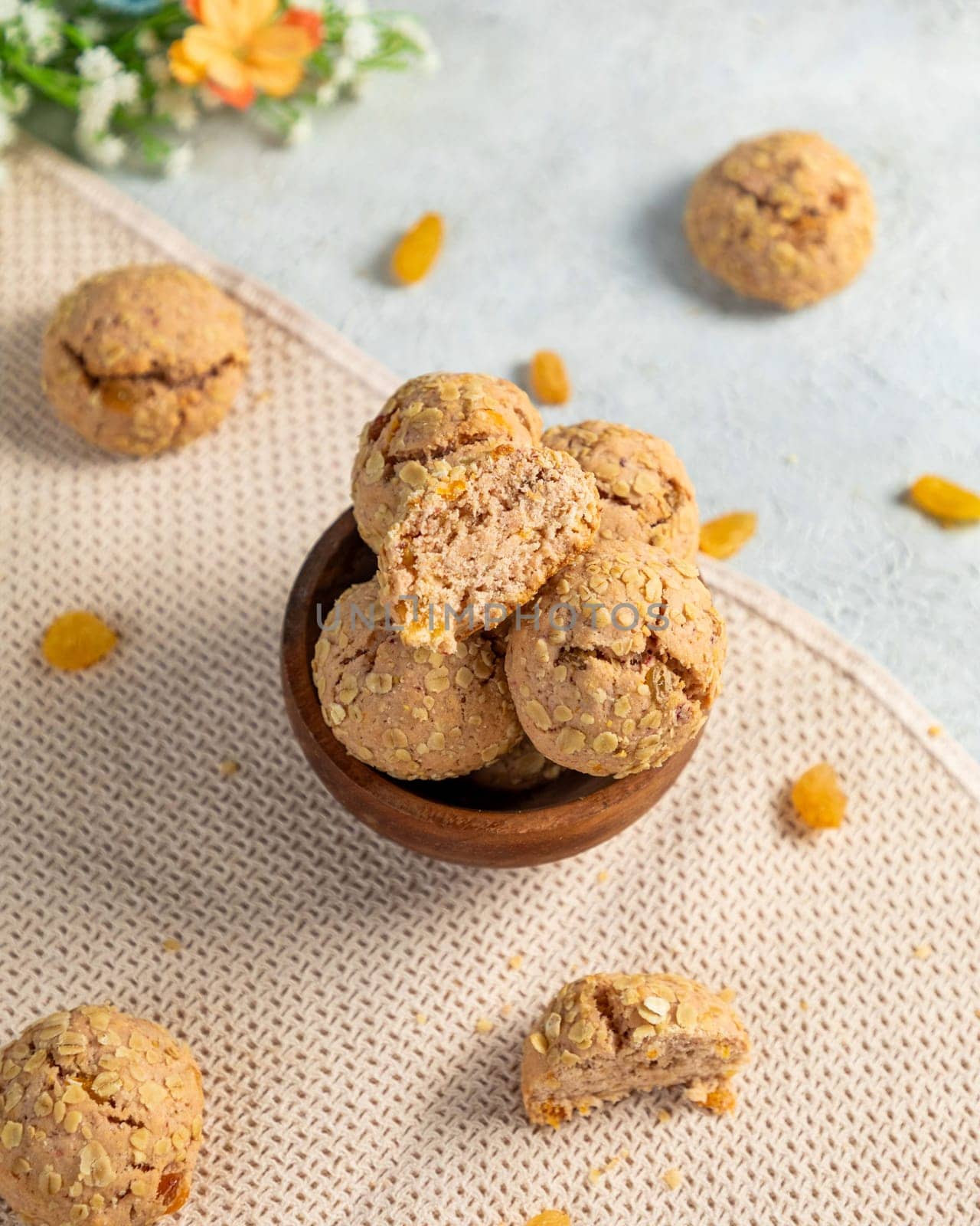 Oatmeal raisin cookies stacked in a wooden bowl, with a few cookies scattered around the bowl