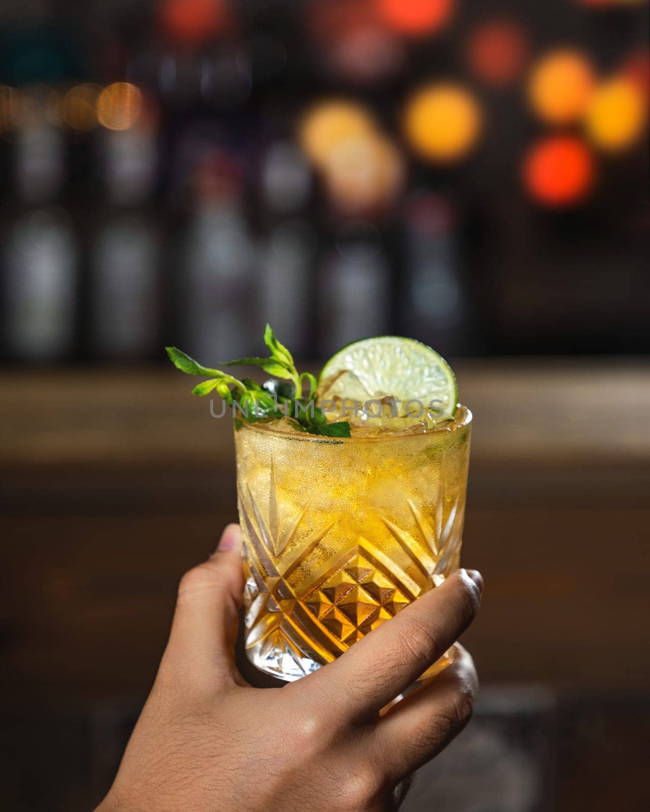 Bartender is holding a refreshing whiskey cocktail with lime and mint against a blurred bar background