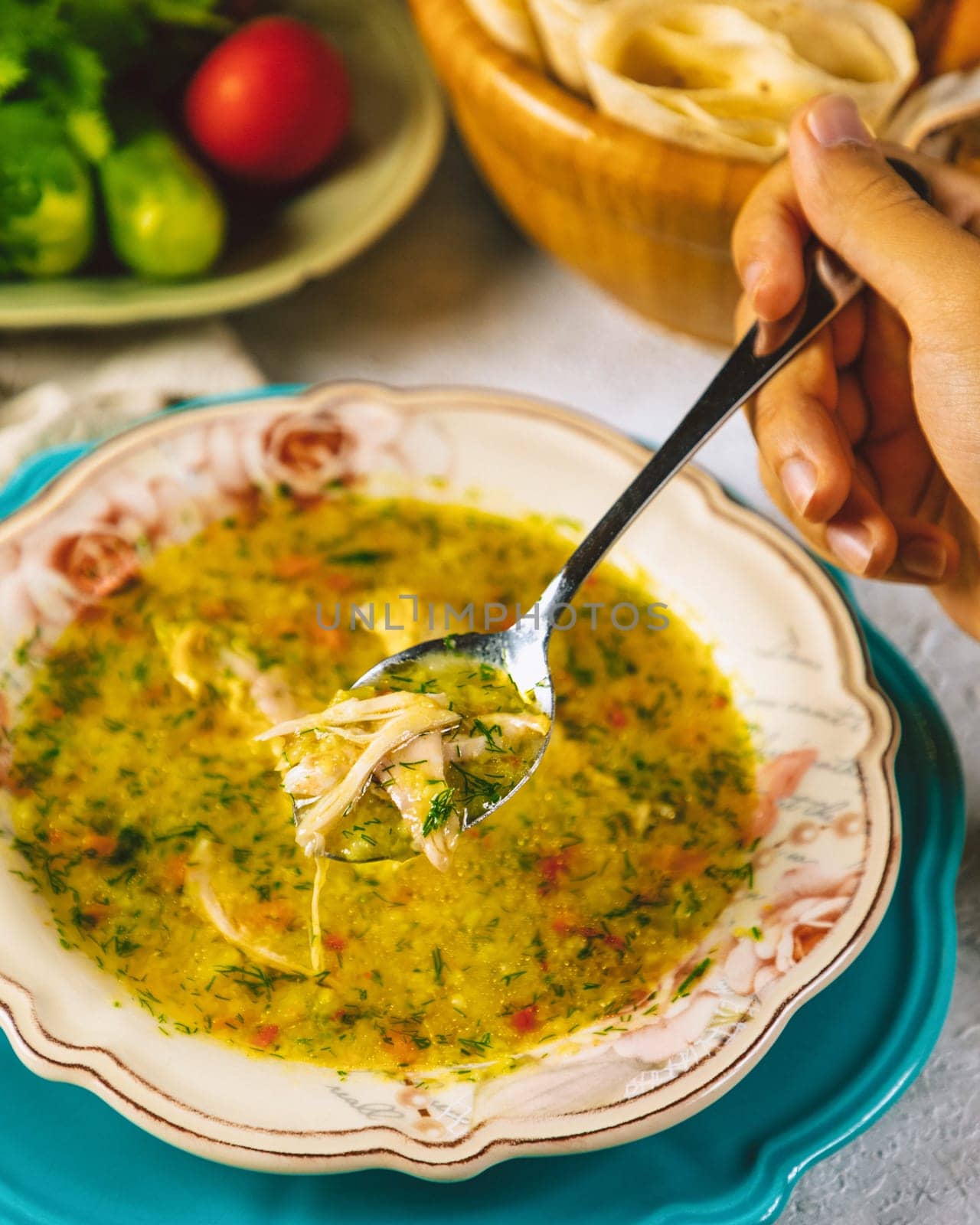 Person holding a spoon with chicken soup over a bowl on a table