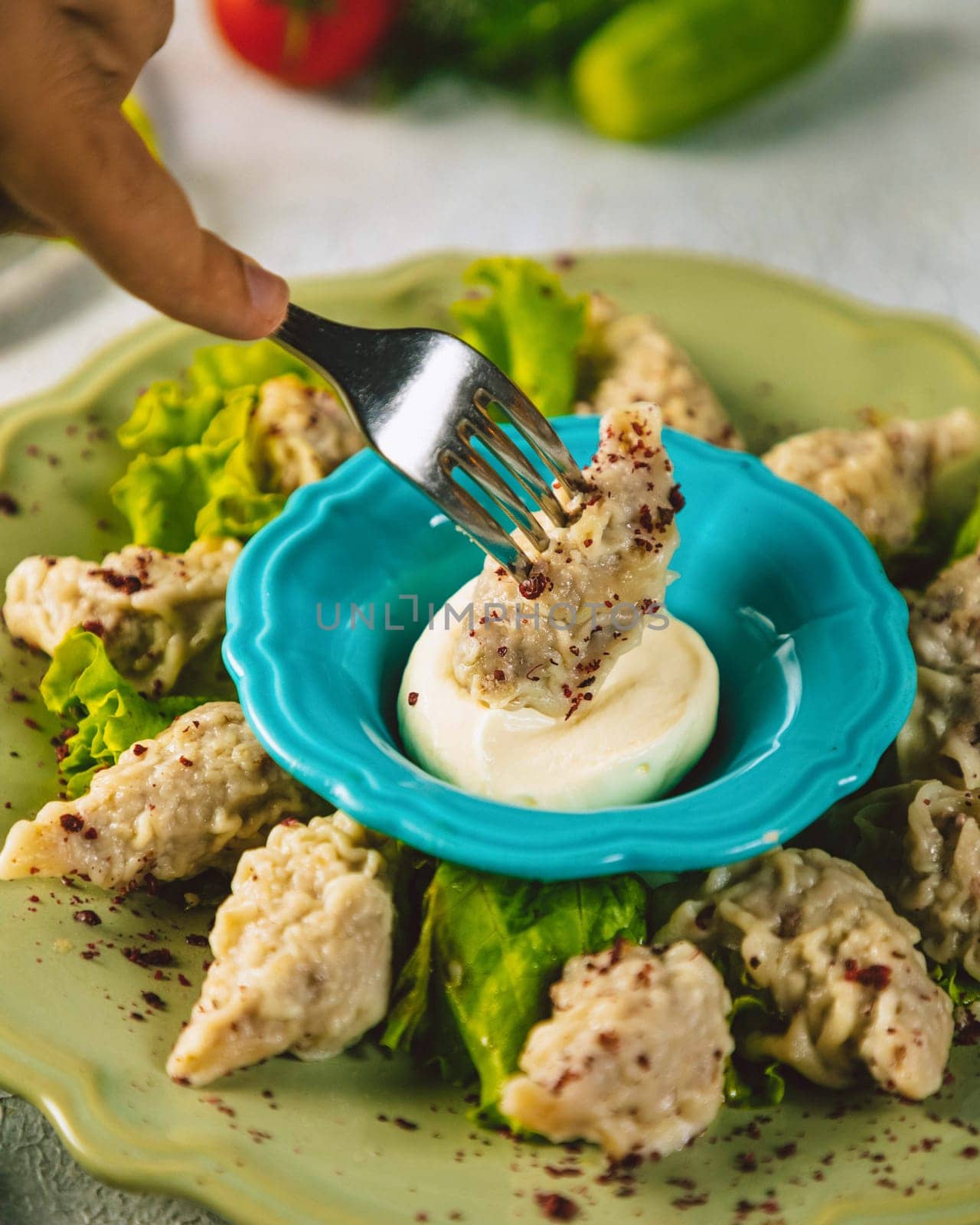 Person is picking up a manti dumpling with a fork from a plate with a blue bowl of yogurt sauce
