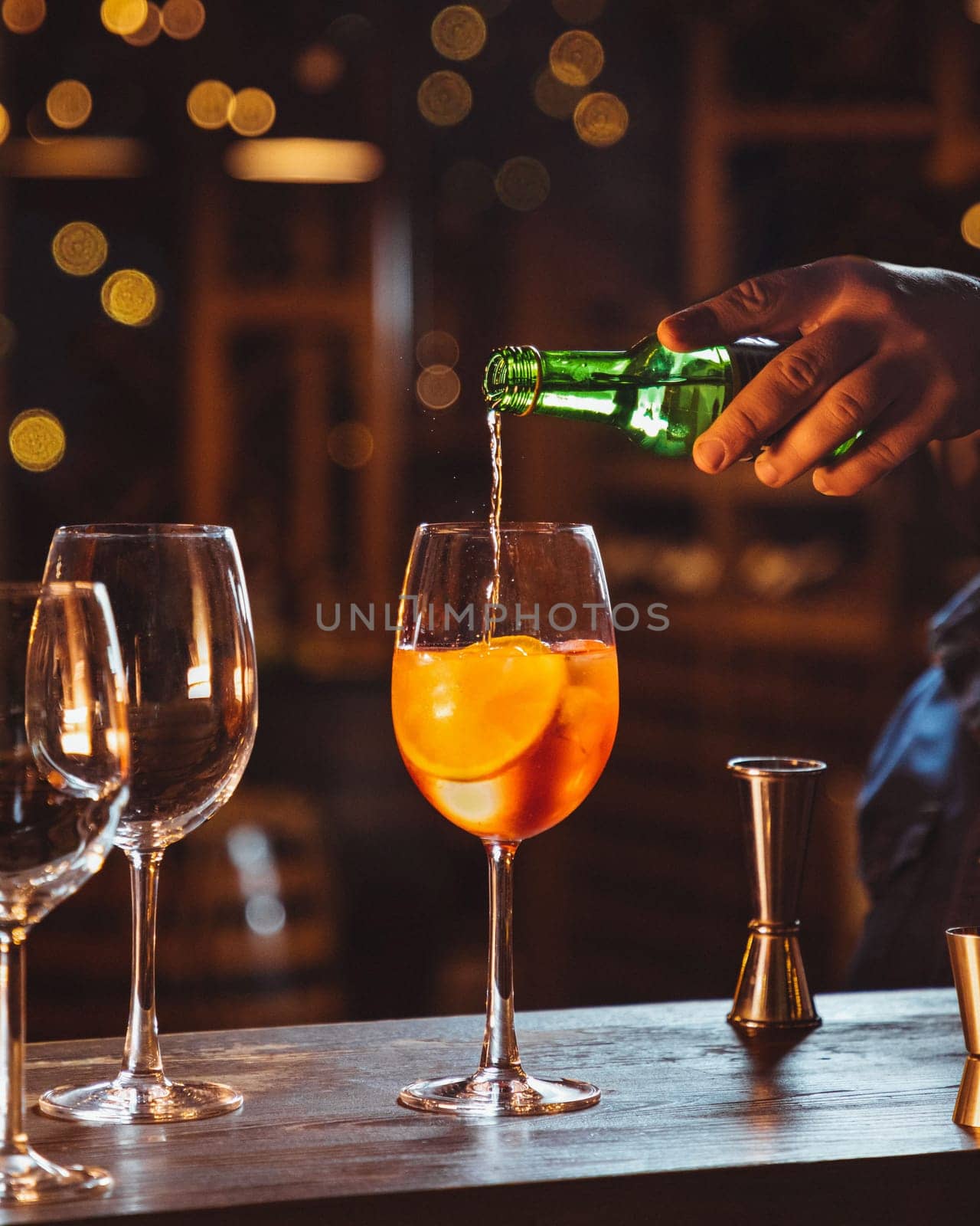Bartender is pouring an alcoholic drink into a cocktail glass containing ice cubes and orange slices
