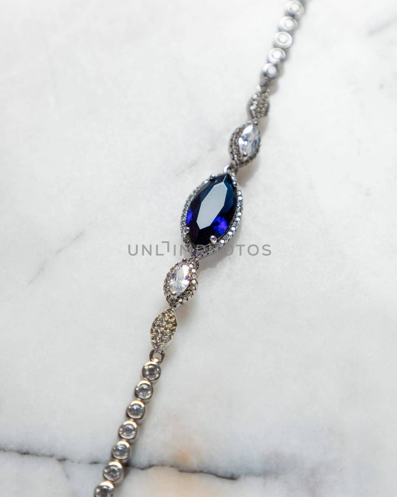 Elegant bracelet with a large blue gemstone as its centerpiece, lying on a white marble surface