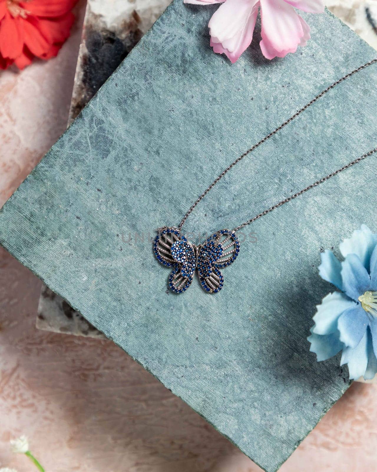 Silver necklace with a butterfly pendant decorated with blue sapphires, photographed on a textured stone