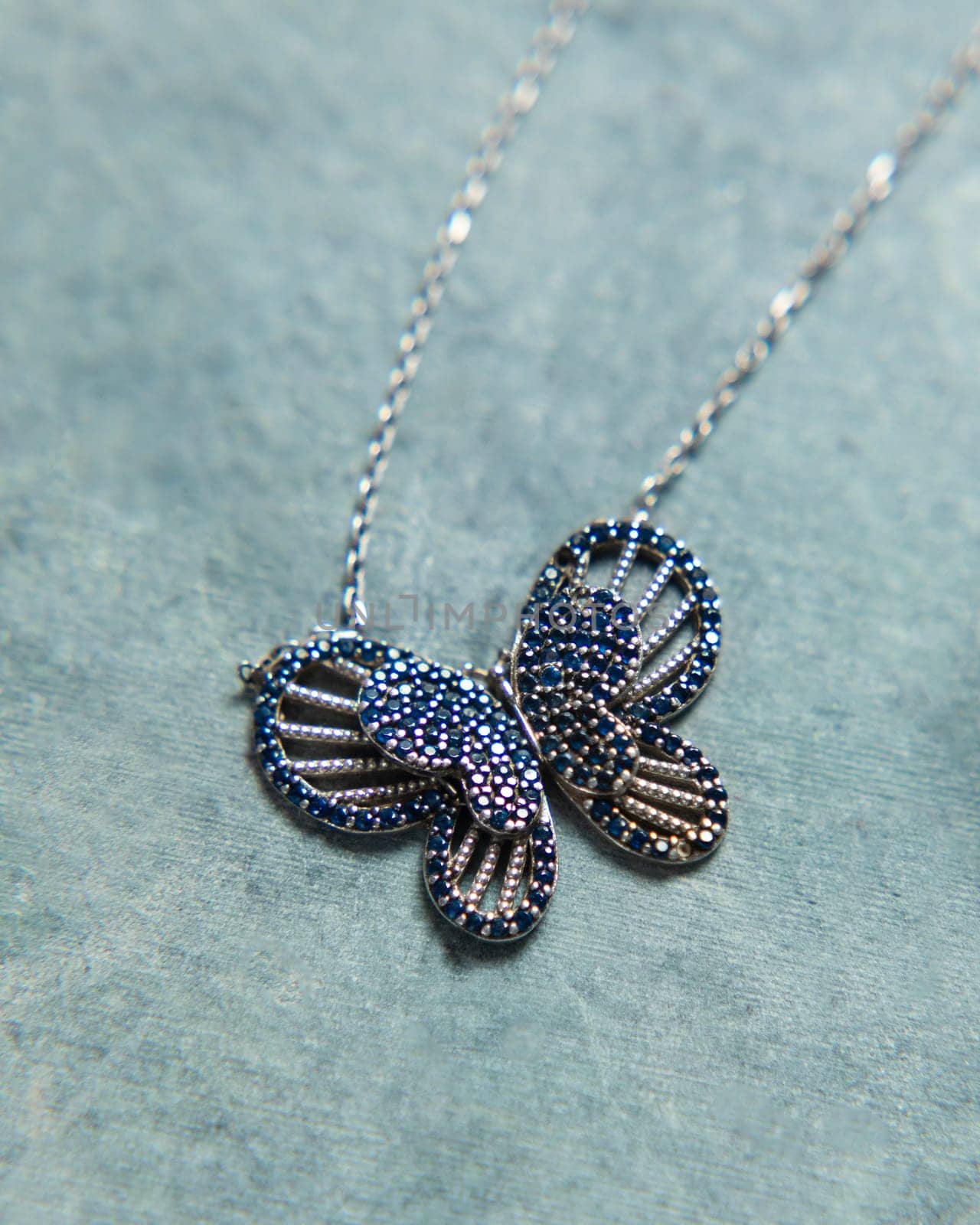 Silver necklace with blue gems forming a butterfly shape, placed on a blue background