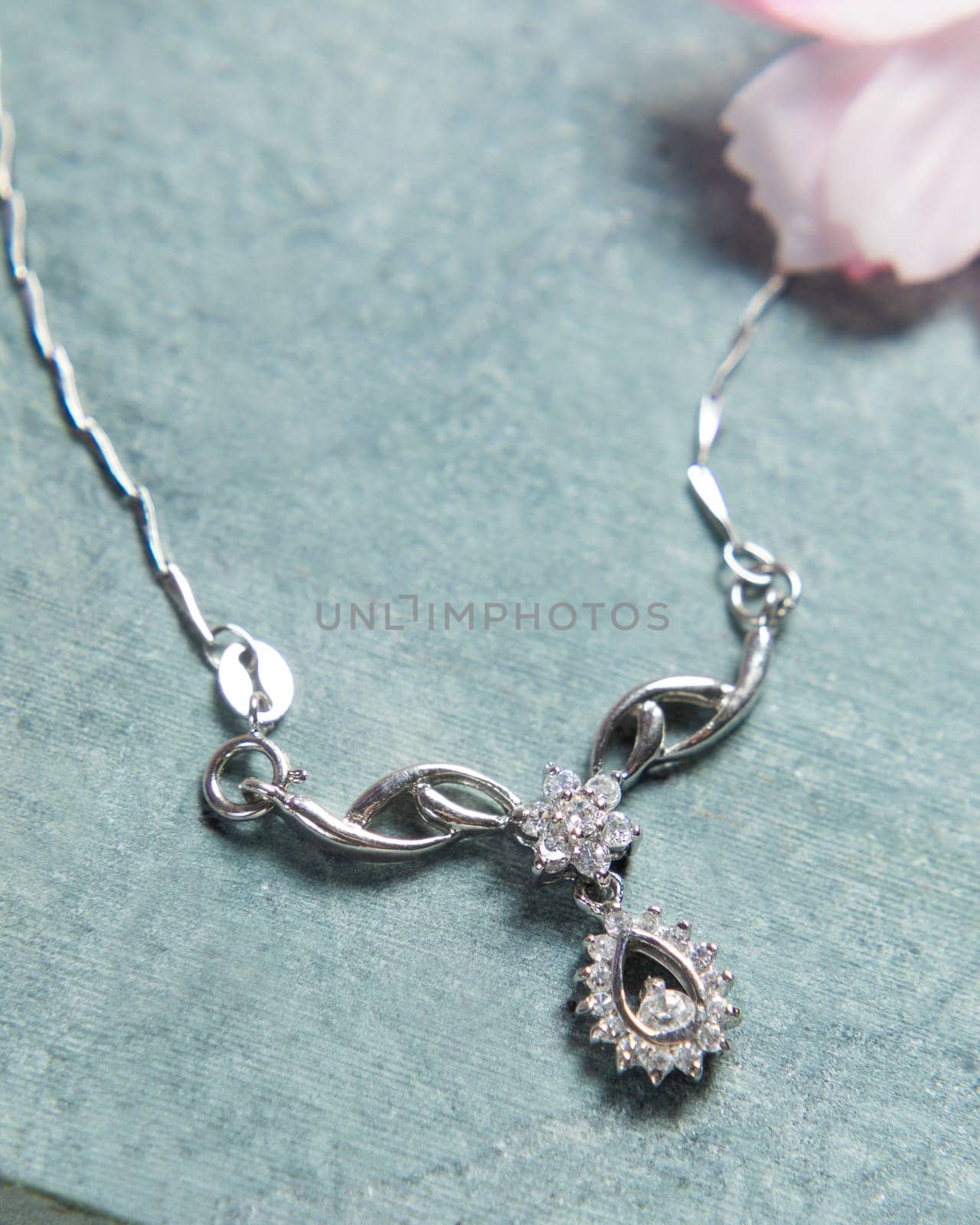 Elegant silver necklace with diamonds on blue background decorated with flower petals