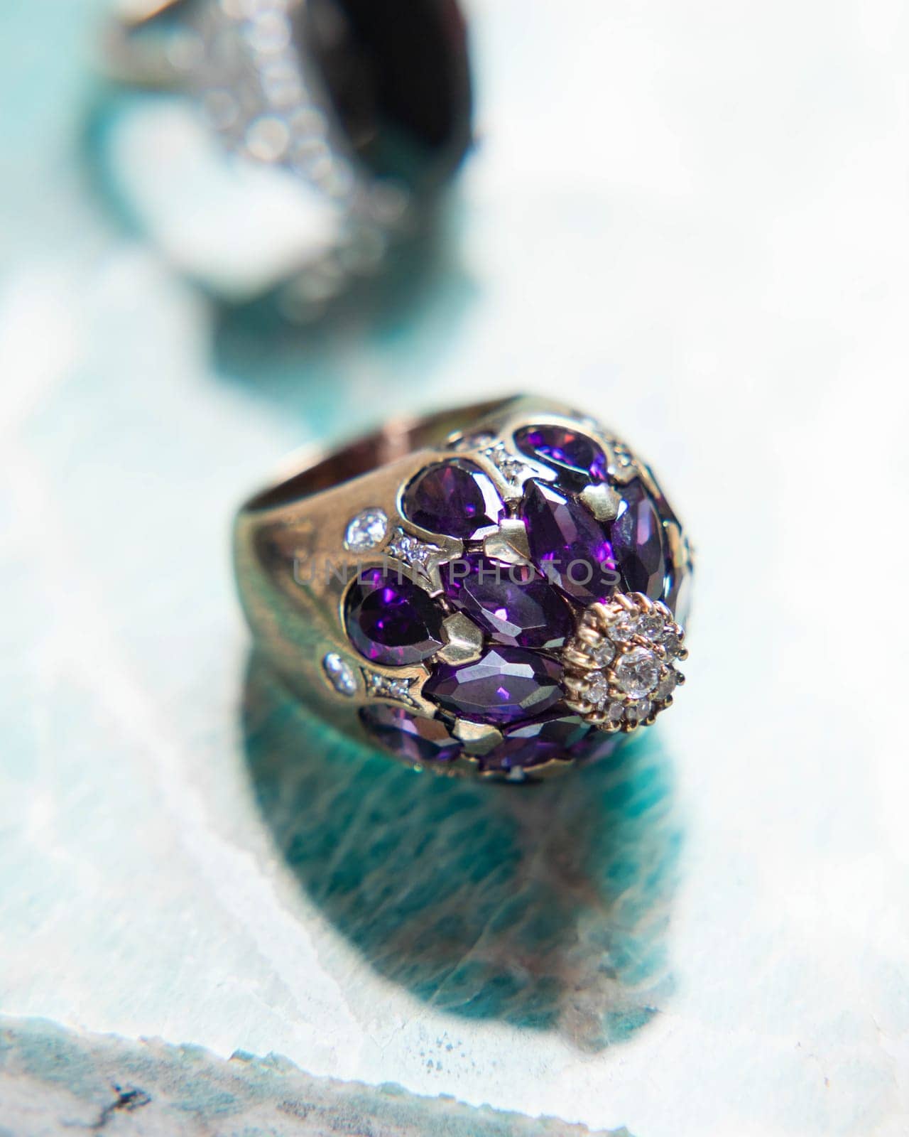 Gold ring with purple amethyst and diamonds on turquoise background, ideal for showcasing luxury and elegance