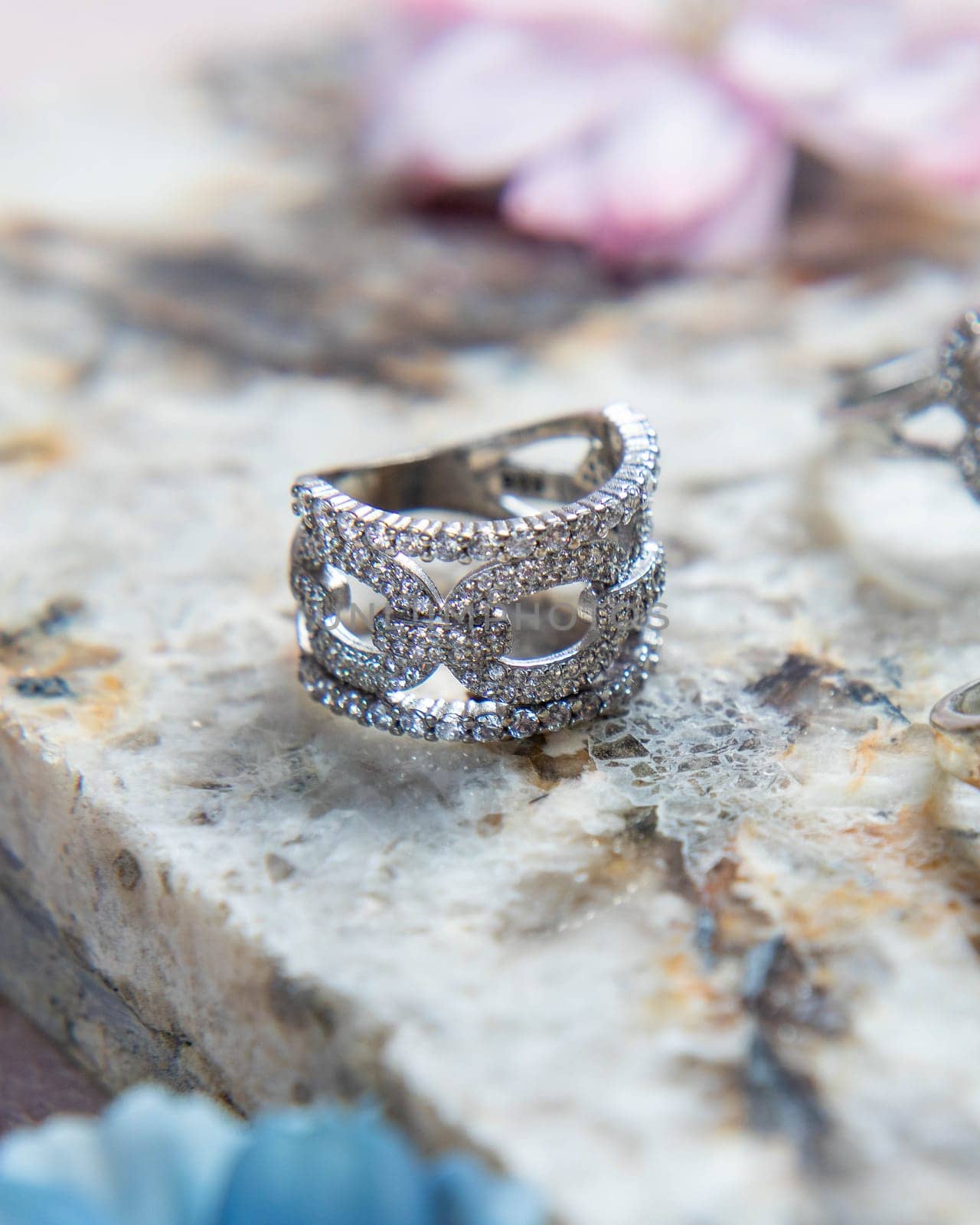 Silver ring with diamonds on stone surface with flowers out of focus in the background