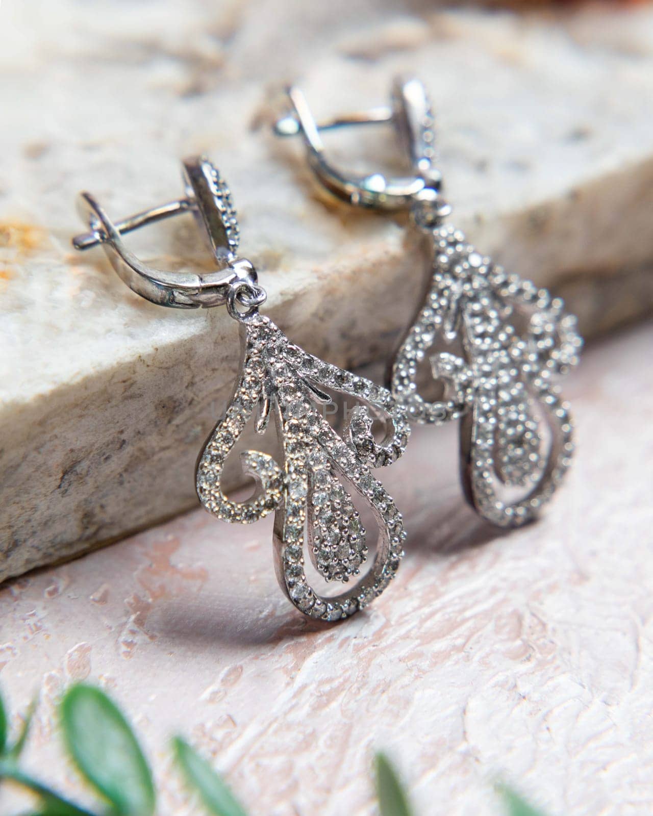 Beautiful sparkling silver earrings with numerous embedded diamonds resting on a stone surface