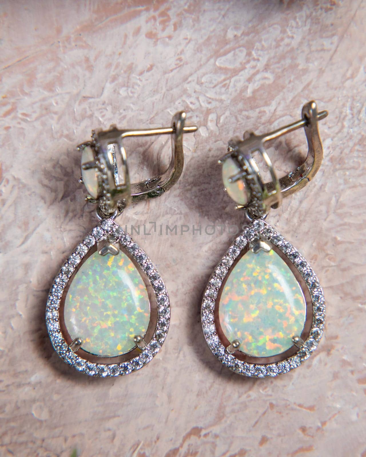 Pair of elegant earrings with a large drop-shaped opal and small diamonds is lying on a textured background