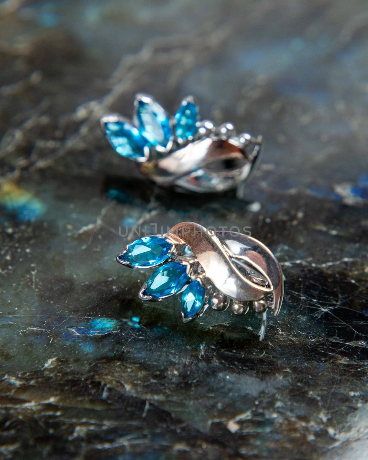 Pair of silver earrings with blue topaz lying on dark stone surface