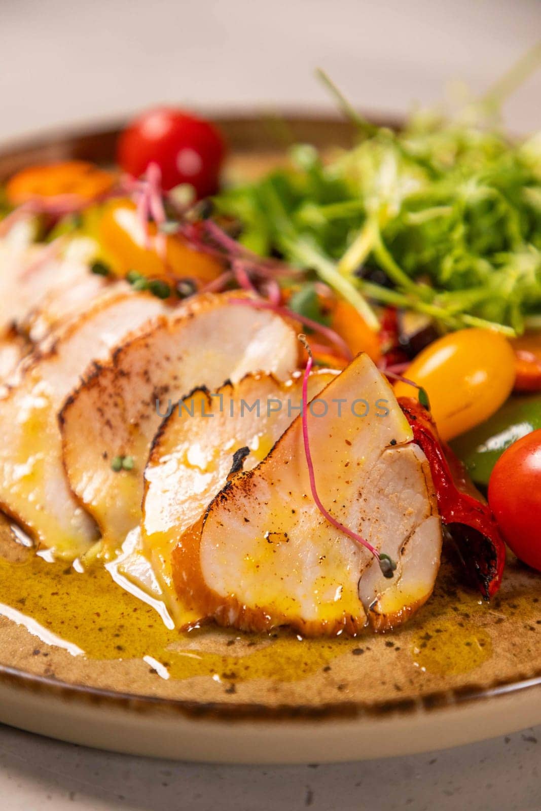 Sliced grilled chicken breast is served on a plate with fresh salad and mustard sauce