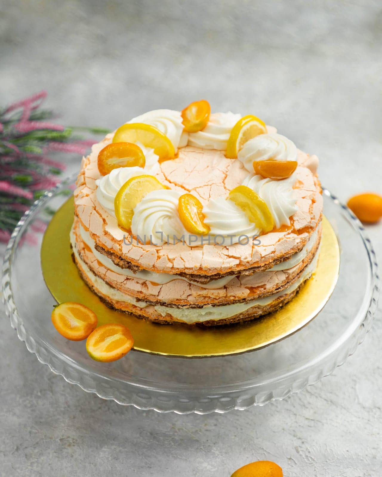 Layered meringue cake with lemon and kumquat slices on top, sitting on a glass serving platter