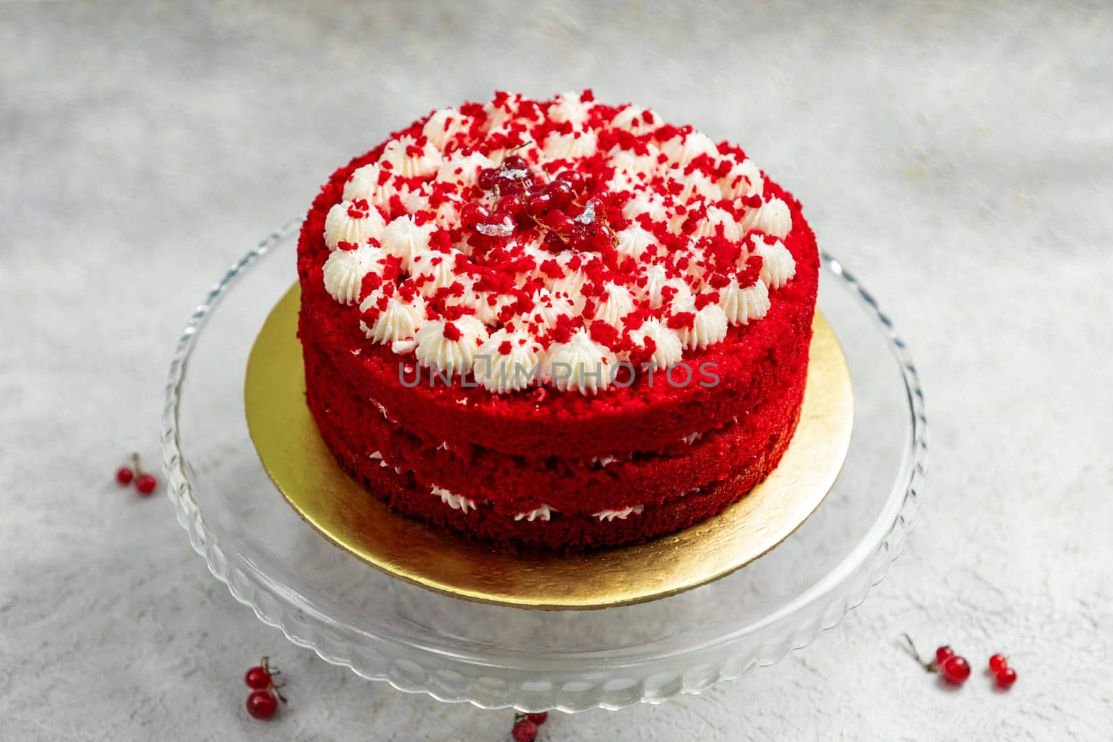 Round red velvet cake with white cream cheese frosting decorated with red currant berries
