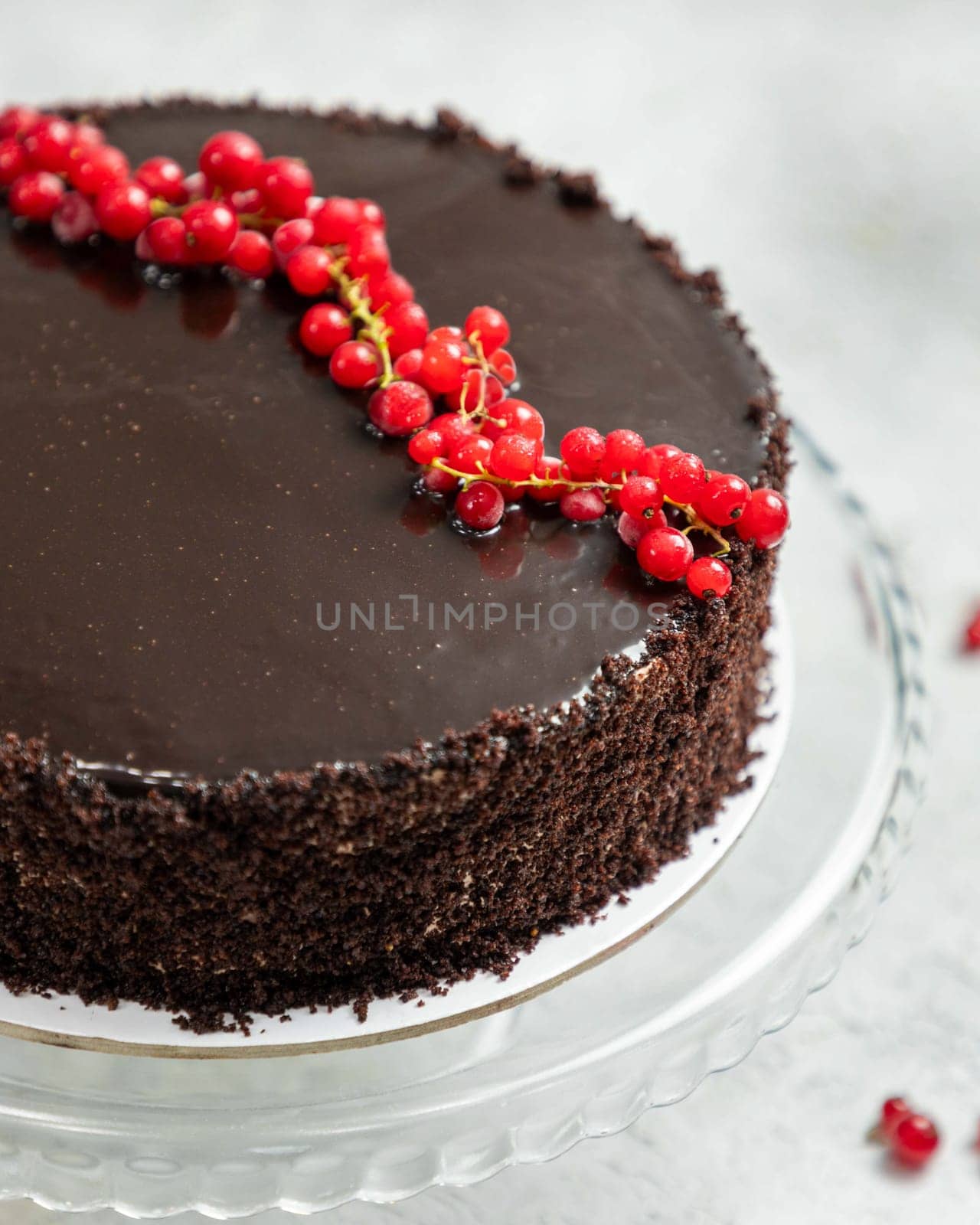 Delicious chocolate cake with chocolate icing being topped with fresh red currants