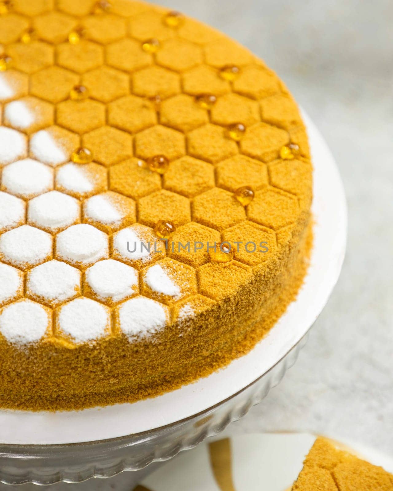 Delicious honeycomb cake with a golden crust decorated with honey drops and powdered sugar standing on a glass plate