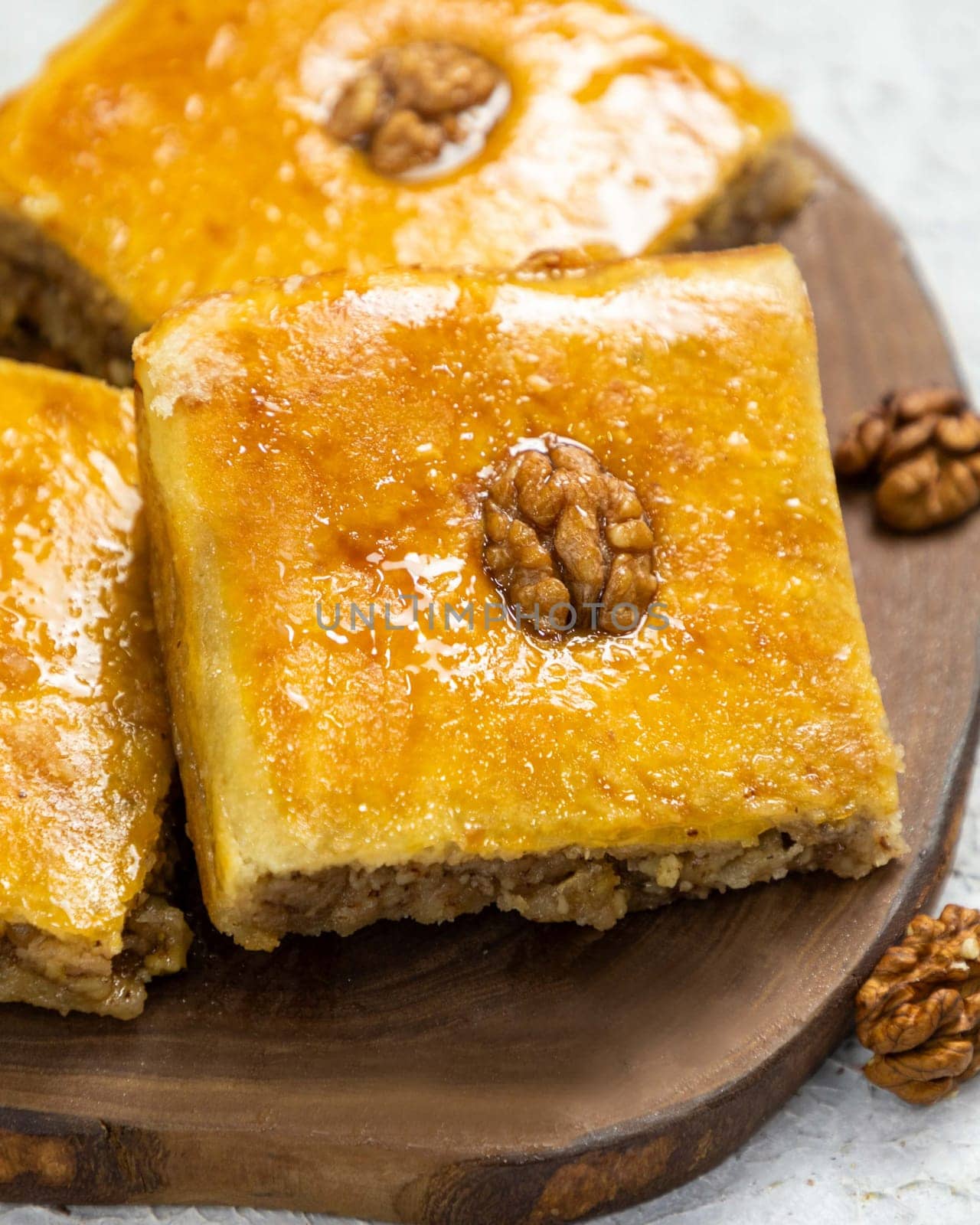 Squares of baklava topped with walnuts are resting on a wooden board