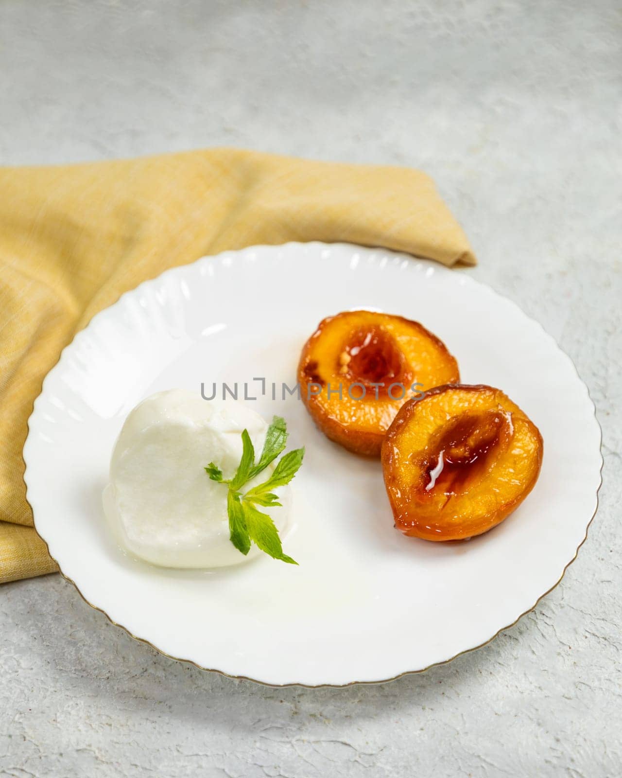 Delicious grilled peach dessert with ice cream and mint on white plate is served on the table