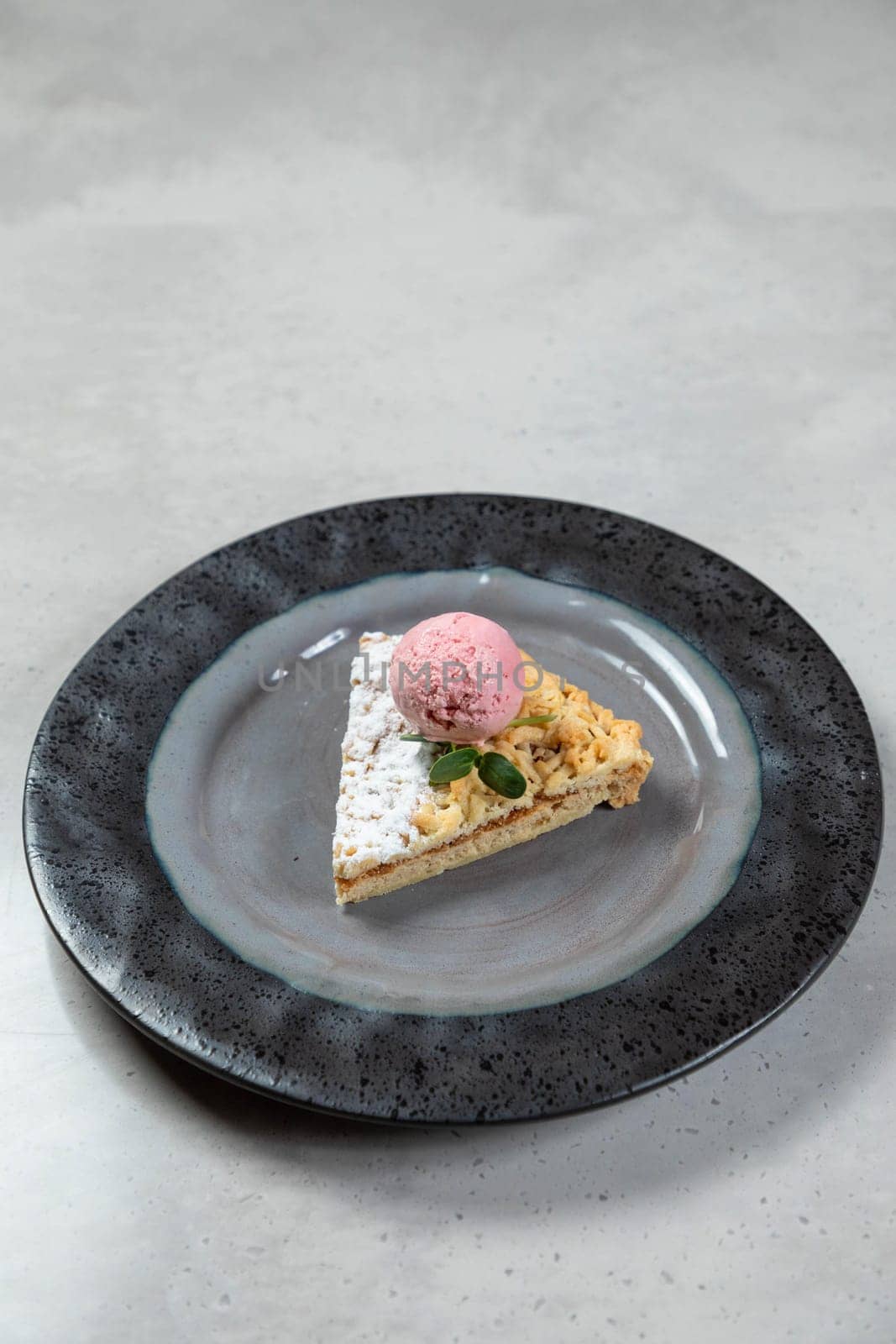 Slice of apple pie topped with vanilla ice cream and powdered sugar sits on a plate