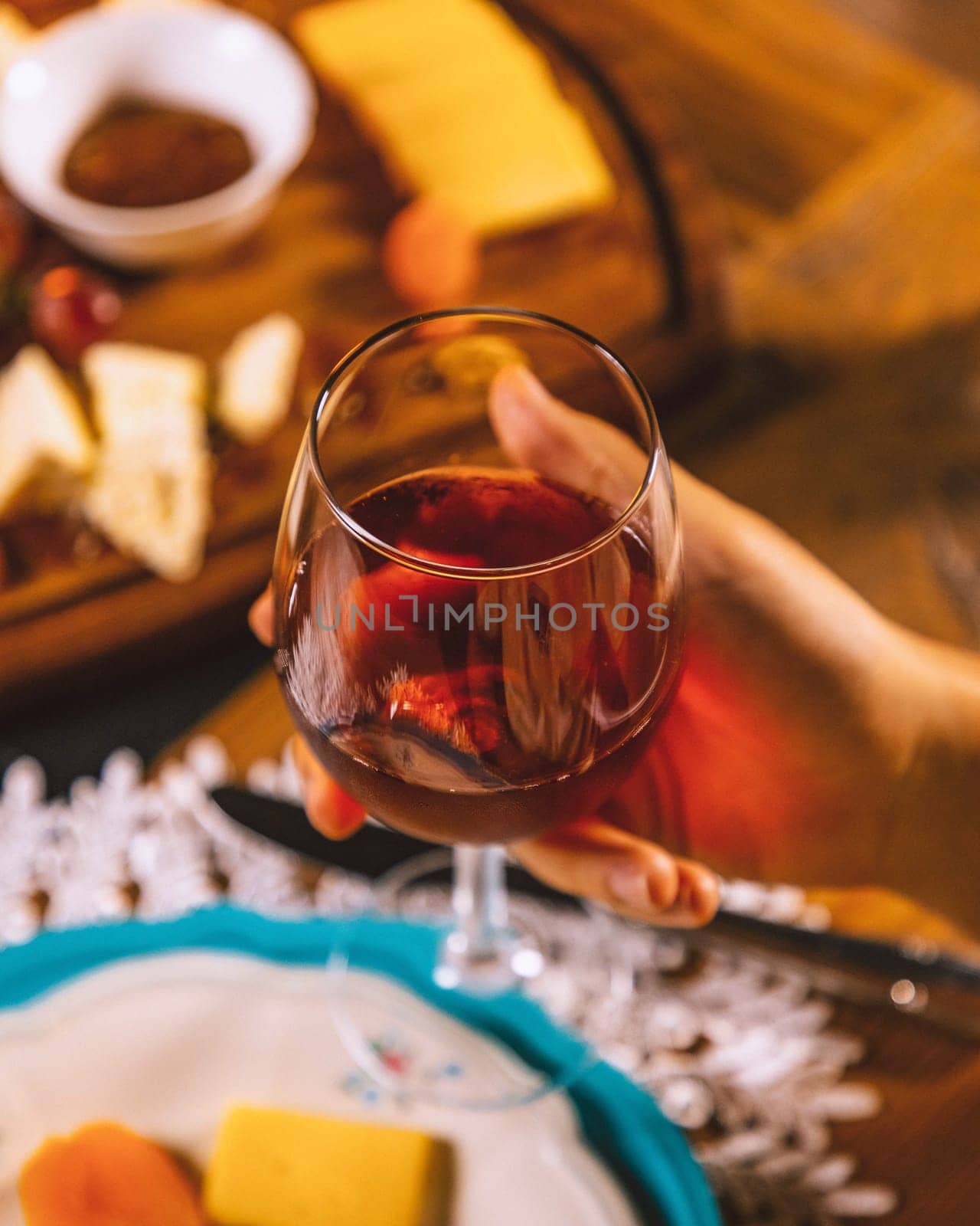 Woman holding a glass of red wine with a cheese board with grapes and honey in the background