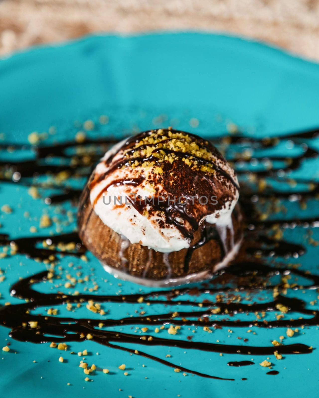Chocolate lava cake topped with vanilla ice cream, drizzled with chocolate sauce and sprinkled with pistachios, served on a turquoise plate