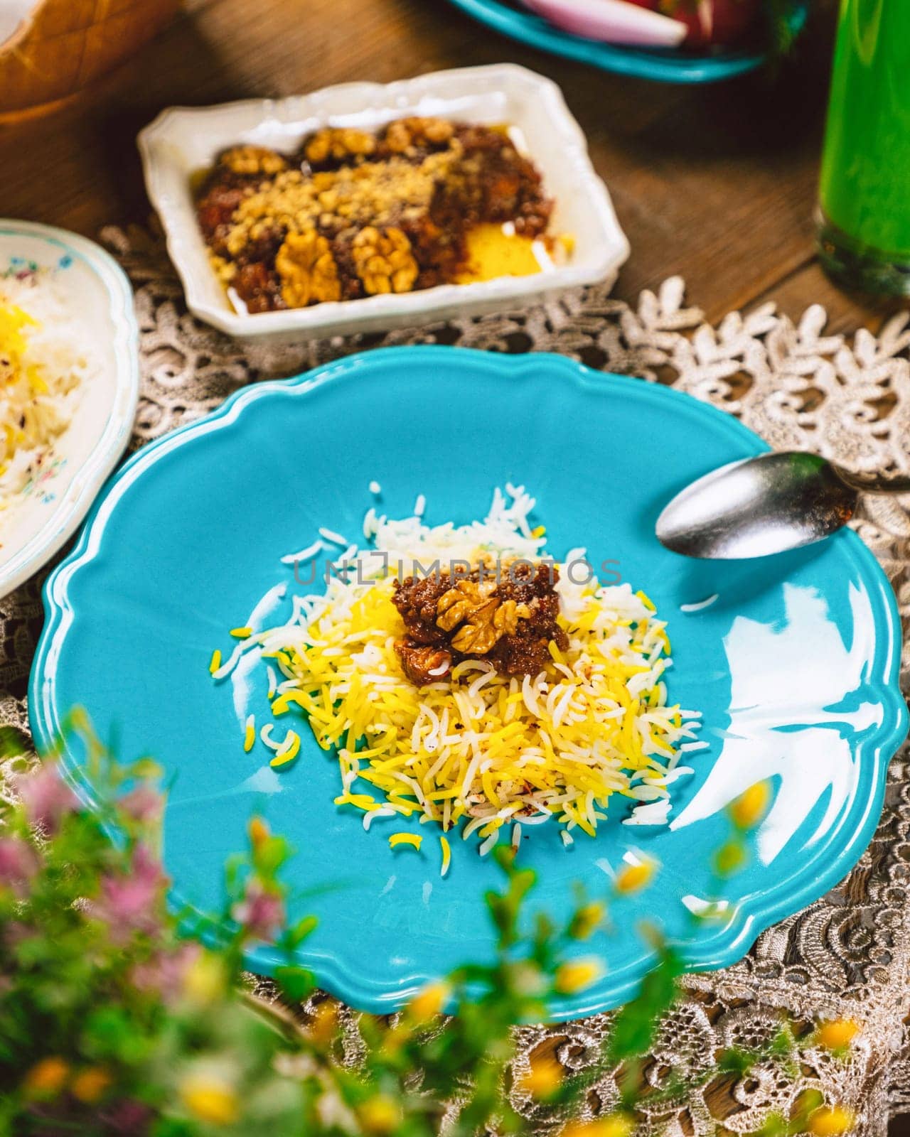 Saffron basmati rice with fesenjan stew made of chicken, walnuts and pomegranate molasses, served on a blue plate on a decorated table