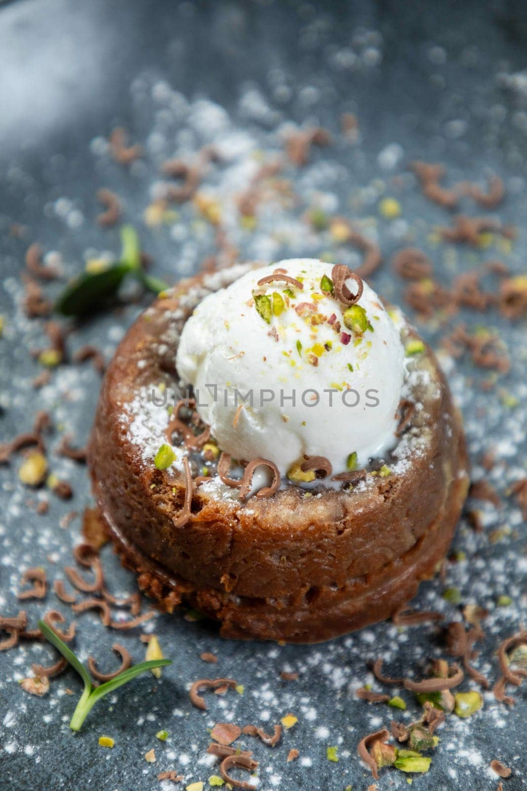 Chocolate lava cake topped with vanilla ice cream, decorated with pistachios and being sprinkled with powdered sugar