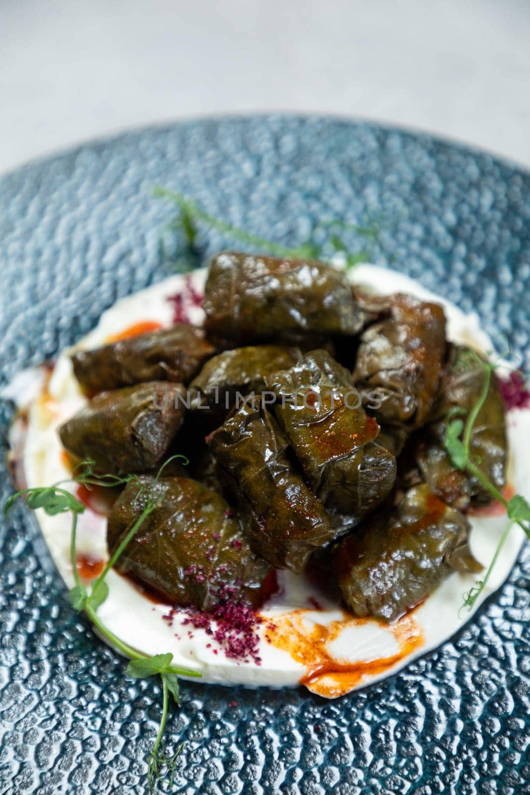 Plate of stuffed grape leaves served with a creamy yogurt sauce and sprinkled with red spices