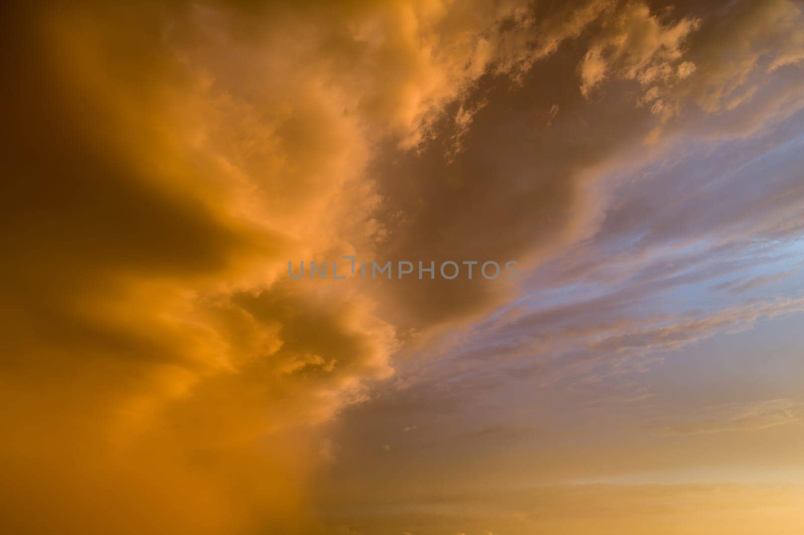 The sky is orange and cloudy. The clouds are low and the sun is setting. The sky is a mix of orange and blue