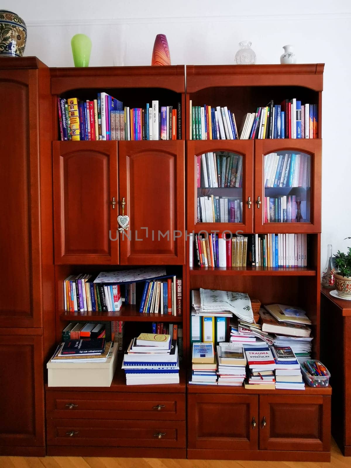 A wooden bookshelf stands in a cozy room, displaying shelves filled with books of various sizes and subjects. Decorative items enhance the inviting atmosphere.