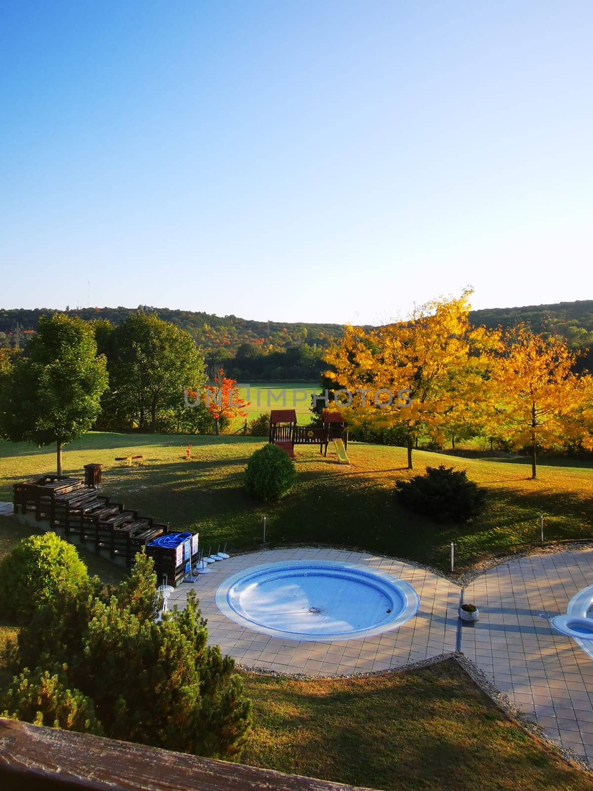 A serene outdoor landscape showcases two inviting hot tubs surrounded by vibrant autumn foliage under a clear blue sky. Perfect for relaxation.