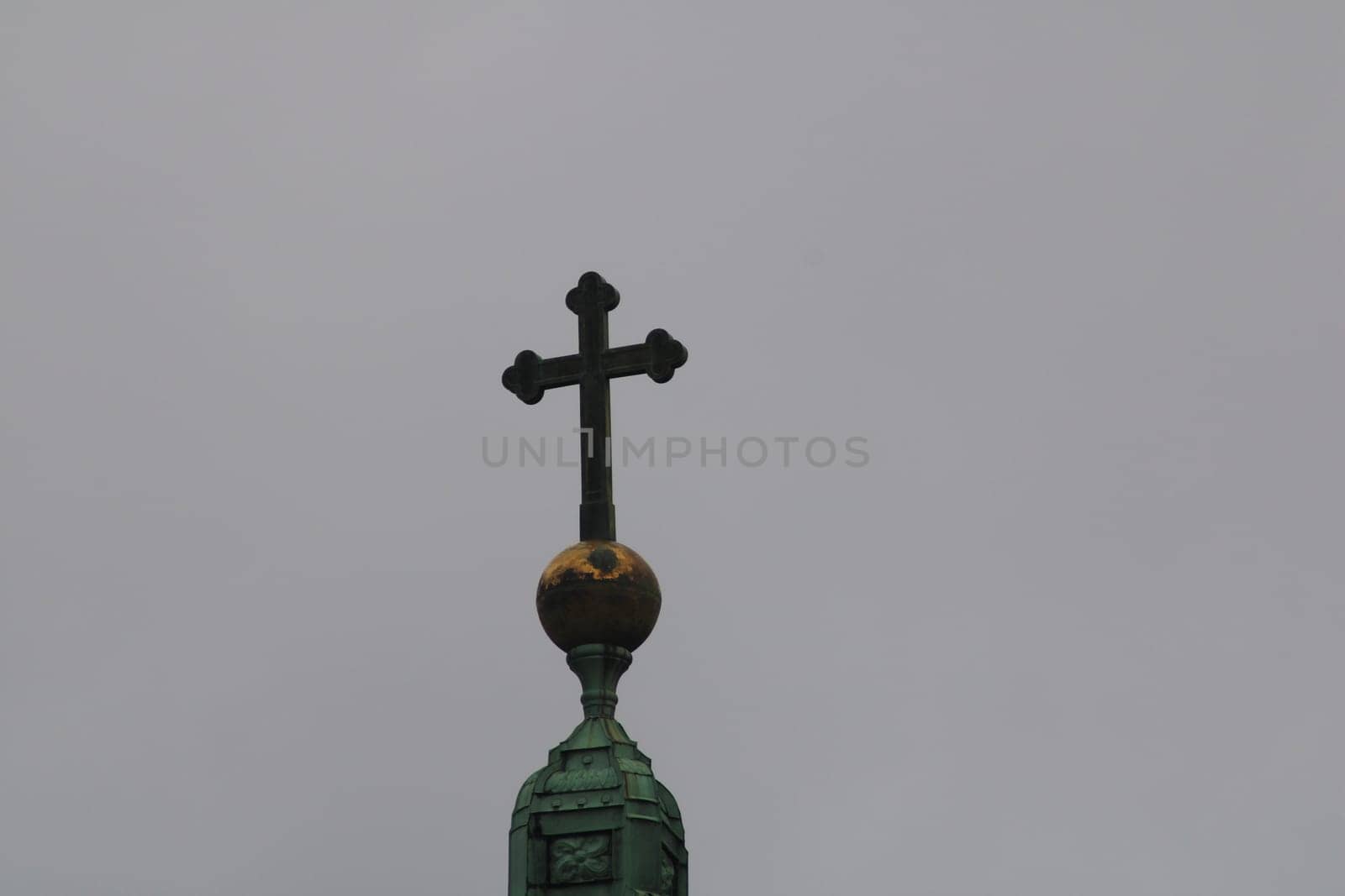 A cross is prominently featured on top of a church spire, with a grey sky providing a dramatic backdrop. The structure symbolizes faith and architectural elegance.