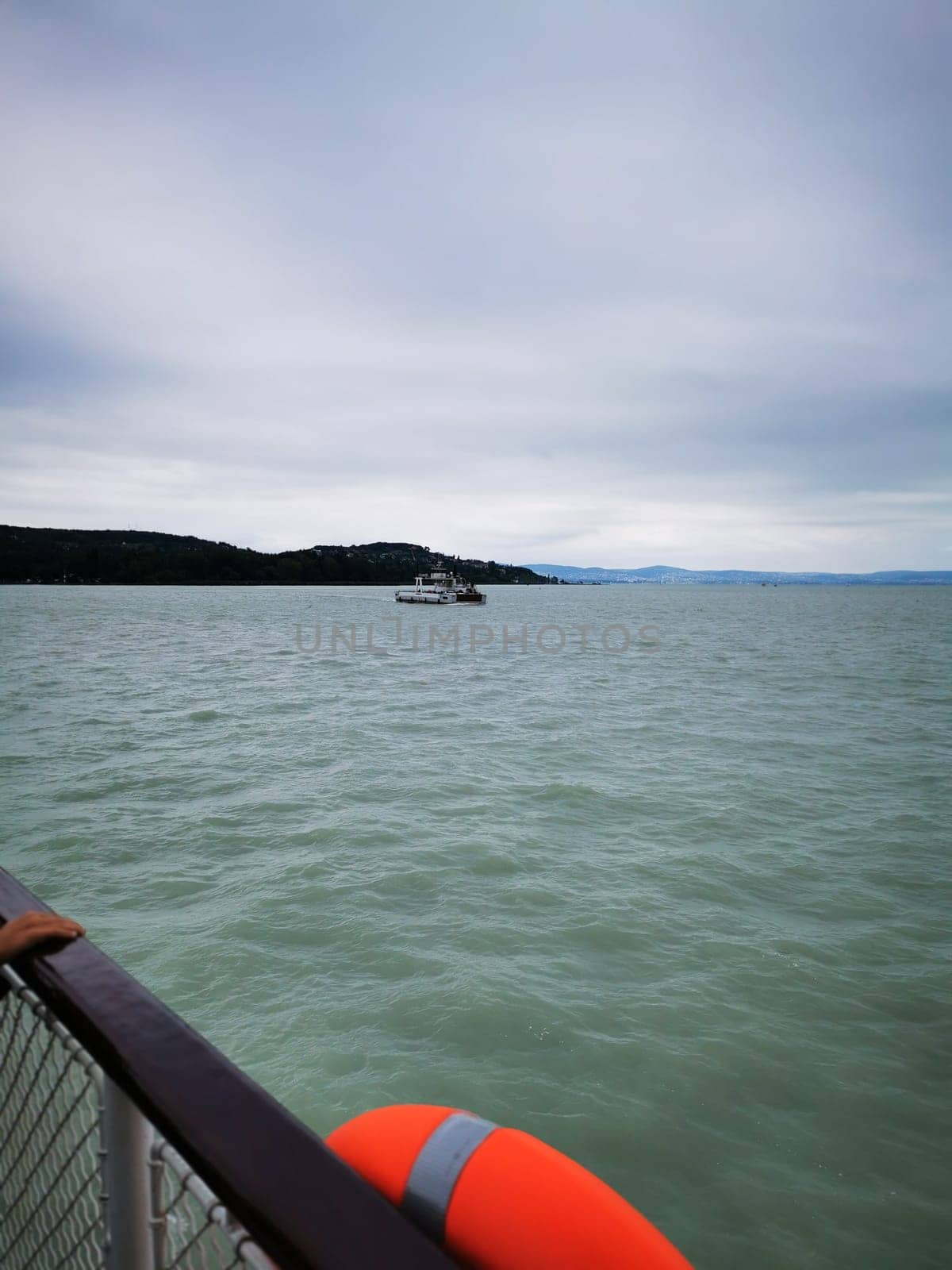 A small boat glides through the tranquil waters, approaching an island surrounded by gentle waves and a backdrop of overcast skies in the afternoon light.
