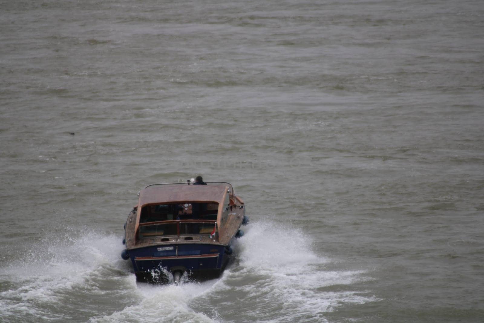 A speedboat plows through rough waters, producing splashes as it moves swiftly. The overcast sky adds a dramatic backdrop to this exciting maritime scene.
