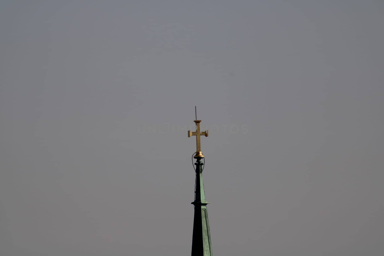 A tall church steeple rises prominently with a golden cross atop, glistening softly in the early morning sun while the sky appears hazy and peaceful.