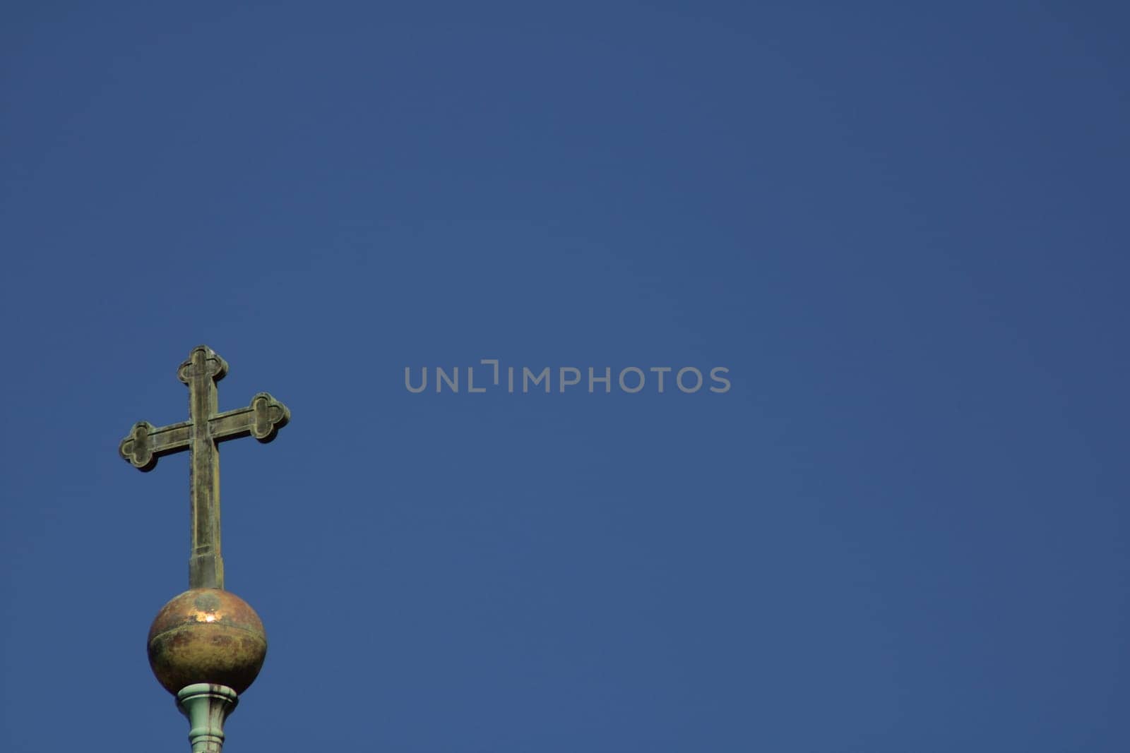 The view captures a tall cross atop a dome set against a bright blue sky, representing faith and tranquility. The scene evokes a sense of peace and devotion.