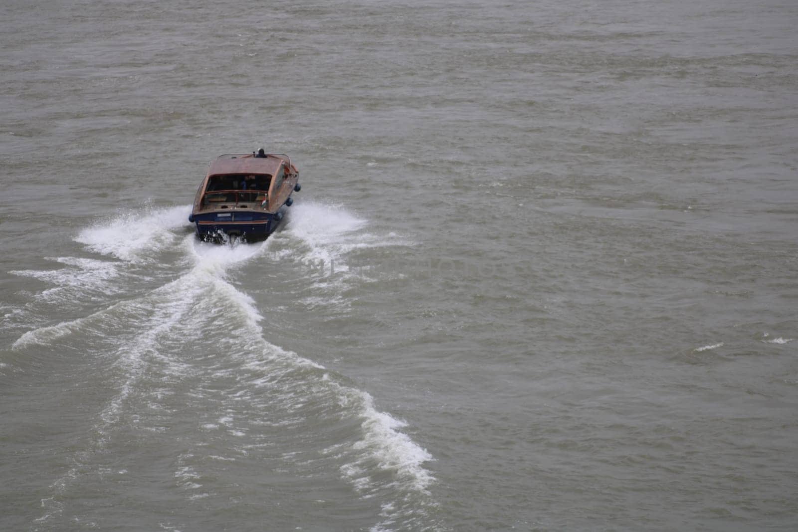 A small boat navigates through tranquil waters under a cloudy sky, leaving behind a series of soft ripples and trails in its wake, showcasing a peaceful journey.