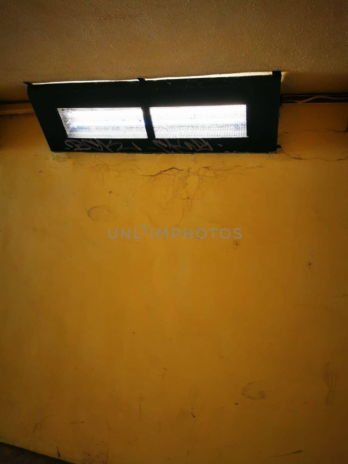 Two rectangular lights cast bright illumination on a plain yellow wall, enhancing the simplicity of the space during the day.
