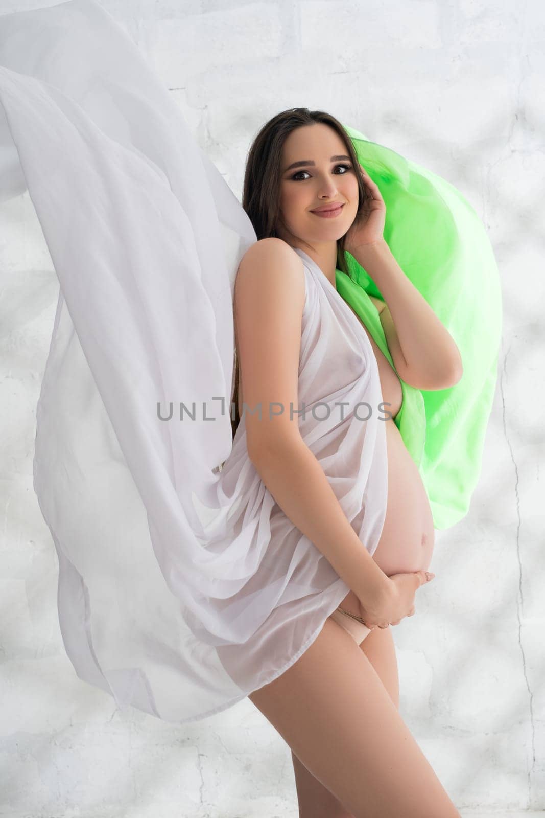 Happy pregnant brunette wrapped in color cloth cropped shot in the nude in a sunny room