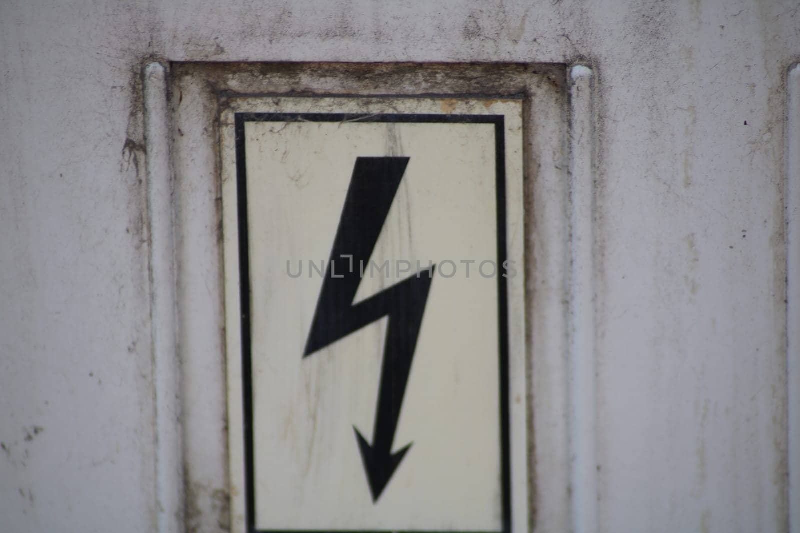A warning sign featuring a stylized lightning bolt symbol clearly indicates the presence of electrical hazards near a building's entrance. Safety measures are highlighted.