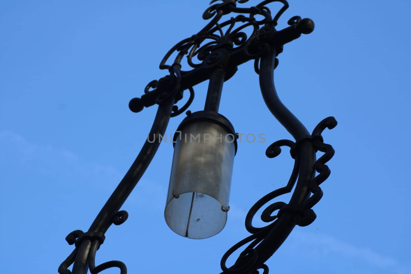 A beautifully crafted street lamp features decorative metalwork and a glass lantern, creating a charming atmosphere on a sunny day, highlighting urban artistry.