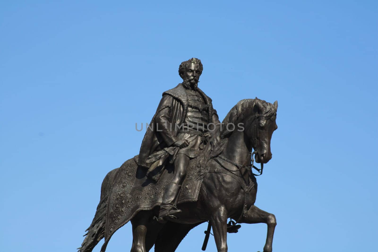 A prominent equestrian statue features a historical figure majestically seated on a horse. The clear blue sky provides a striking backdrop to the artwork.
