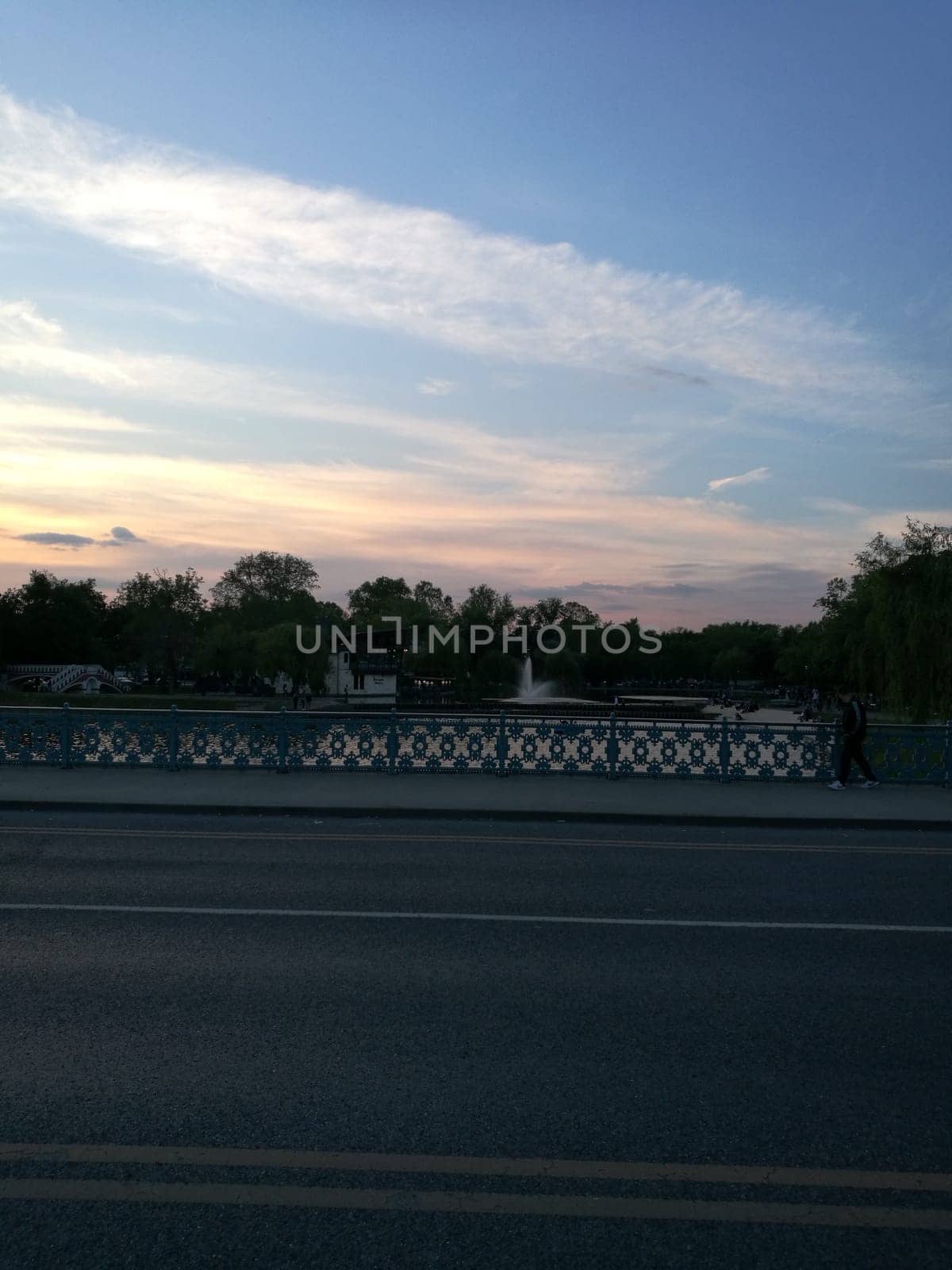 A tranquil scene unfolds at dusk, where a quiet bridge spans a shimmering lake, illuminated by the warm colors of the sunset against a clear sky.