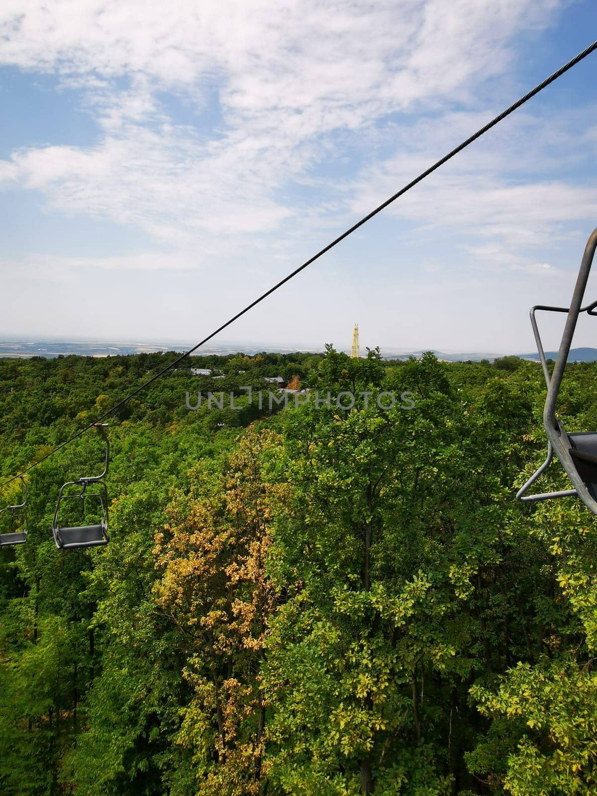 Riding a chairlift provides a breathtaking perspective of verdant trees below and rolling hills in the background under a bright blue sky, revealing nature's beauty.