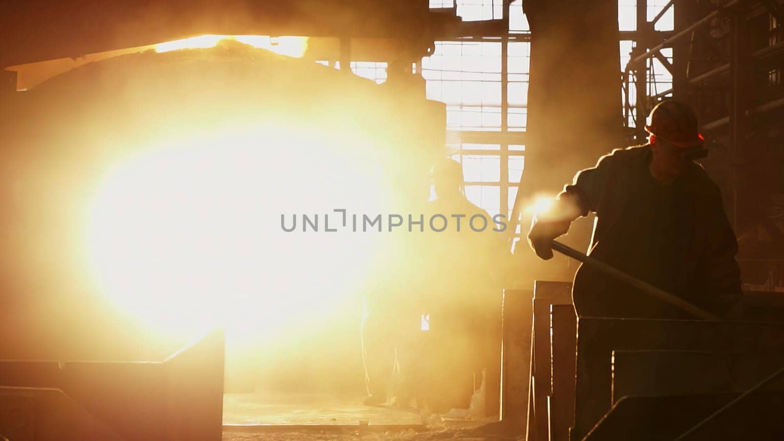 A silhouette of a dedicated worker stands out against a bright, industrial background filled with dust. Stock Clip