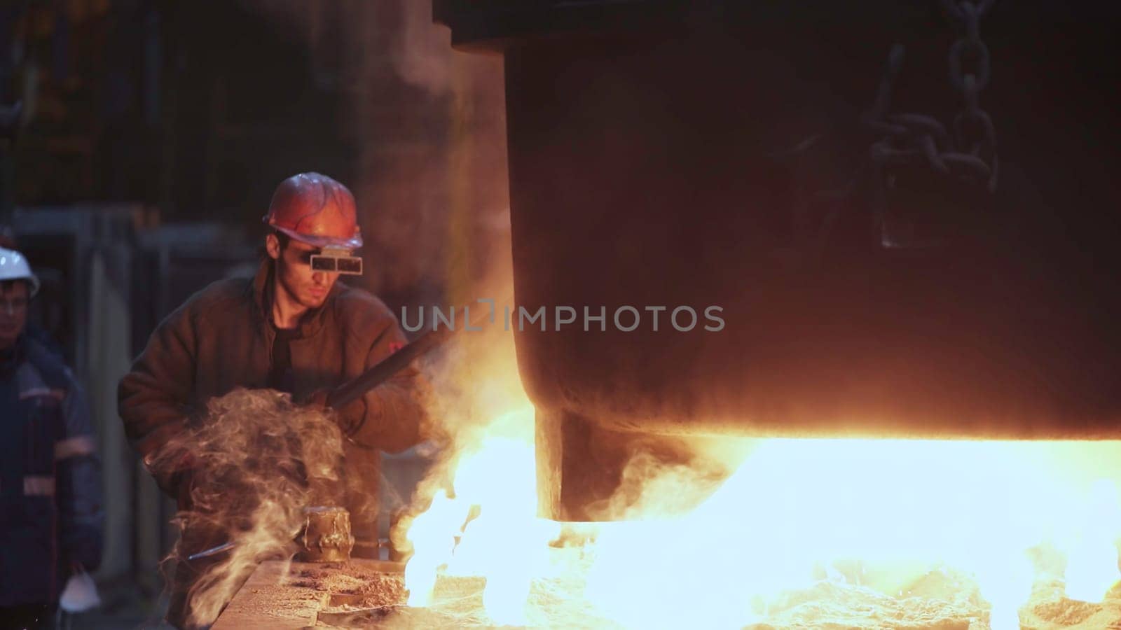 A skilled worker expertly manages molten metal, highlighting the intense nature of industrial manufacturing. Stock Clip