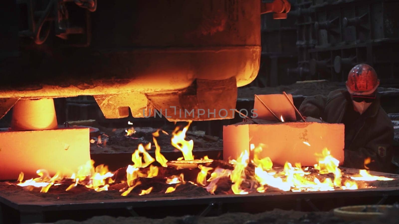 In a dynamic industrial setting, a skilled worker deftly shapes molten metal amidst intense flames and smoke. Stock Clip