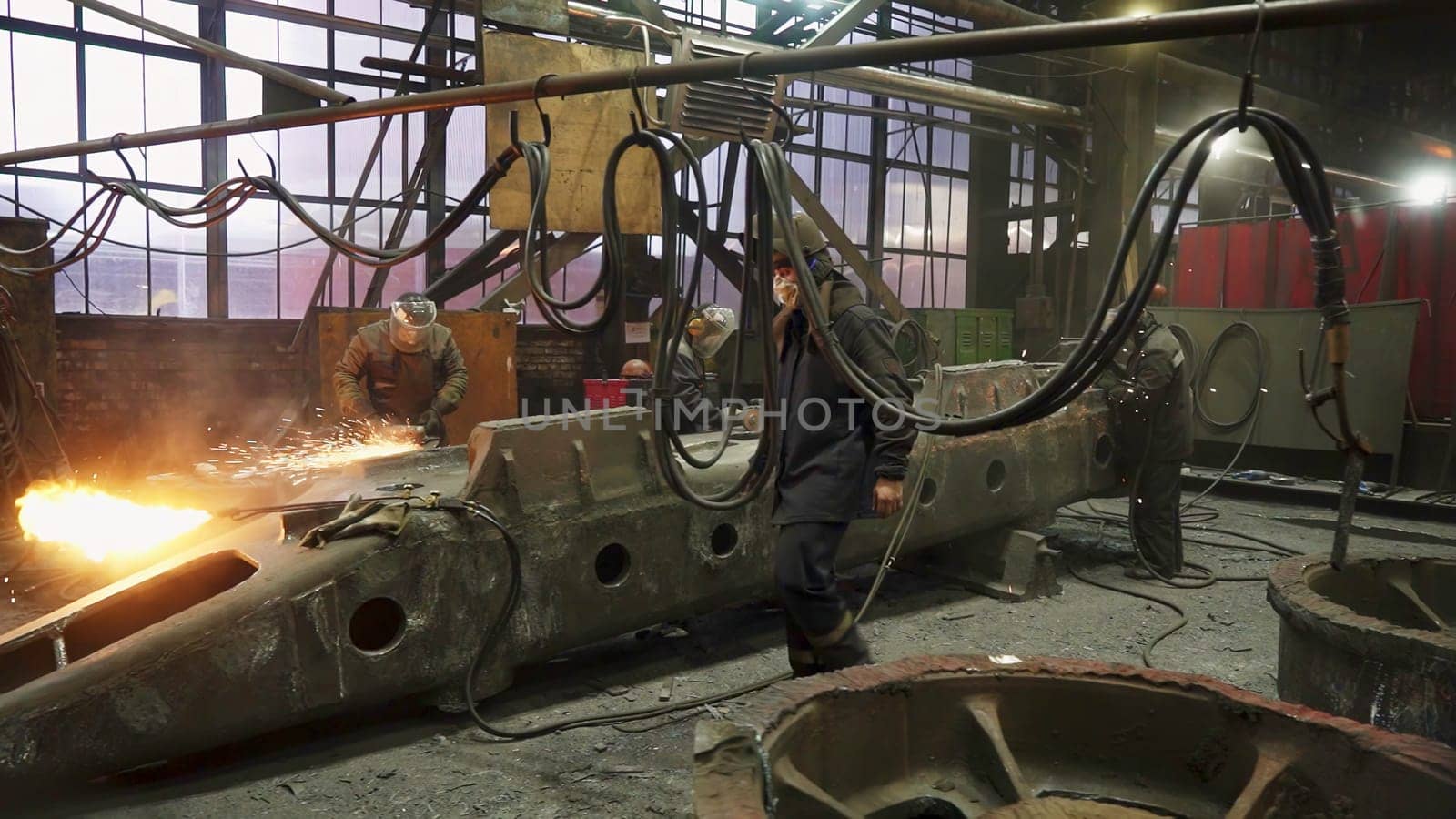 Workers who are engaged in various welding operations inside a large and bustling industrial workshop. Stock Clip