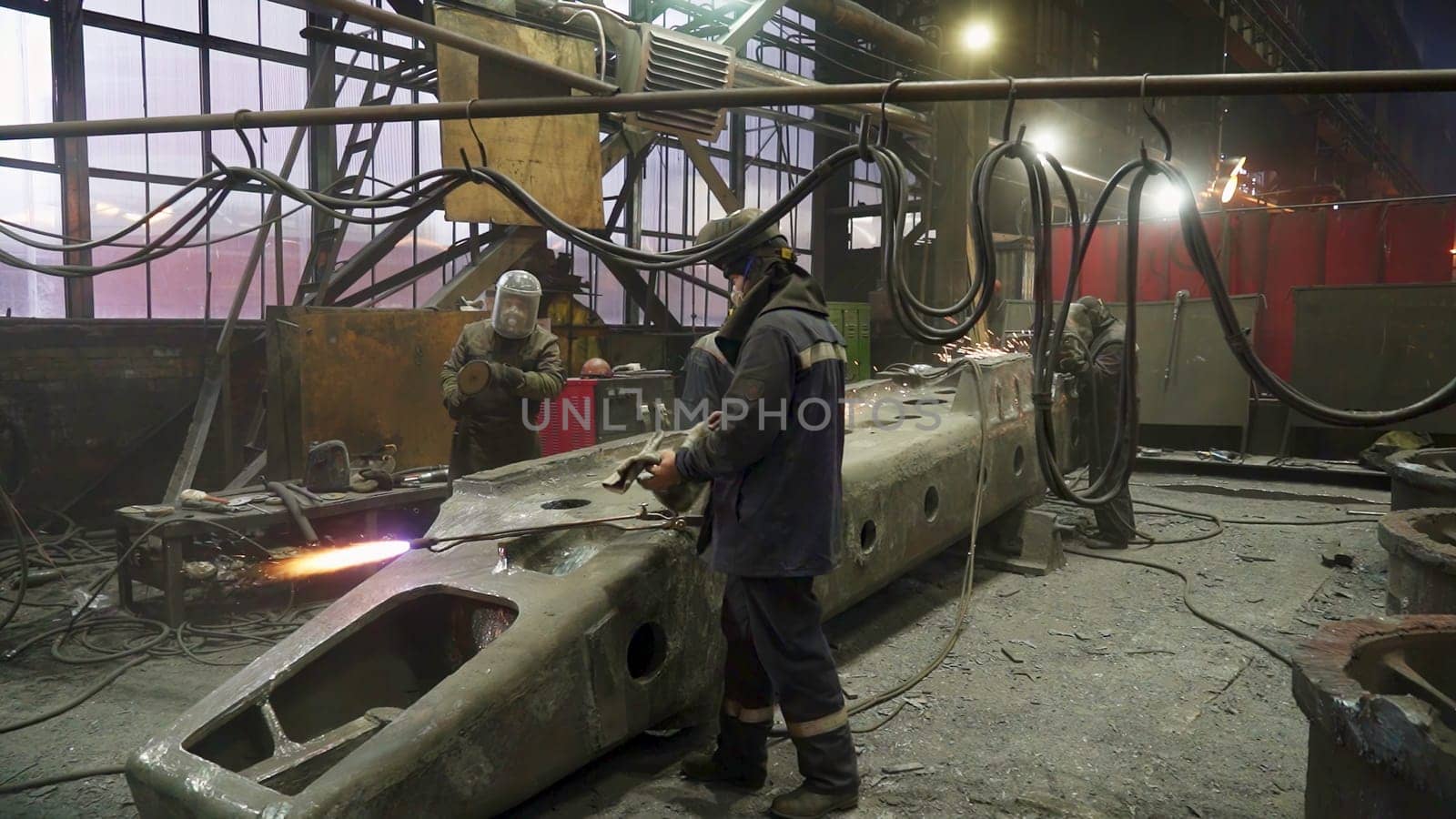Factory workers in an industrial environment diligently creating metal components using specialized welding equipment. Stock Clip